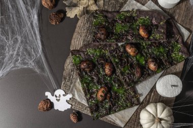 Cadılar Bayramı konsepti. Kalamar mürekkebi, yeşil peynir, mantar ve mor soğanlı düz ekmek ya da pizza. Şenlikli dekorlu, beyaz balkabaklı, mumlu ve örümcek ağlı Ölülerin Ekmeği. Karanlık taş arkaplan