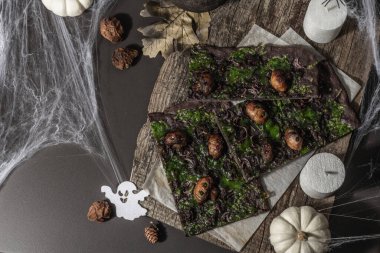 Cadılar Bayramı konsepti. Kalamar mürekkebi, yeşil peynir, mantar ve mor soğanlı düz ekmek ya da pizza. Şenlikli dekorlu, beyaz balkabaklı, mumlu ve örümcek ağlı Ölülerin Ekmeği. Karanlık taş arkaplan