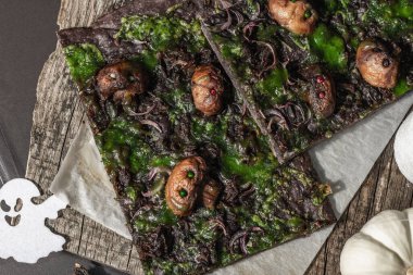 Cadılar Bayramı konsepti. Kalamar mürekkebi, yeşil peynir, mantar ve mor soğanlı düz ekmek ya da pizza. Şenlikli dekorlu, beyaz balkabaklı, mumlu ve örümcek ağlı Ölülerin Ekmeği. Karanlık taş arkaplan