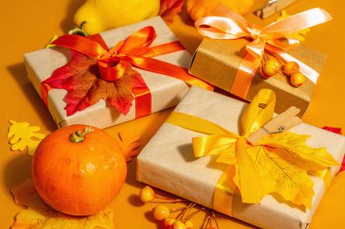 Sonbahar renklerinde hediye konsepti. Paketlenmiş kutular, şenlikli sonbahar dekoru, balkabağı, yapraklar ve böğürtlen. Modaya uygun sert bir ışık, koyu gölge, turuncu arkaplan, kapat