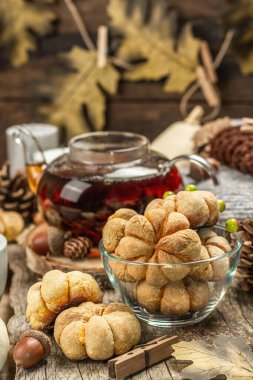 Sonbahar çayı konsepti. Balkabaklı kurabiye, çaydanlıkta siyah çay, sonbahar dekoru. Çelenk, mumlar, rahat bir kazak. Eski ahşap arka plan, kapat