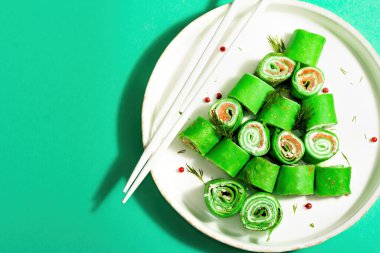 Soğuk meze, Noel ağacı şeklinde süslenmiş. İnce krep, krem peynir, tuzlu somon, yeşiller, modaya uygun sert ışık, koyu gölge. Şenlikli Yeni Yıl dekorasyonu, turkuaz arka plan, üst görünüm