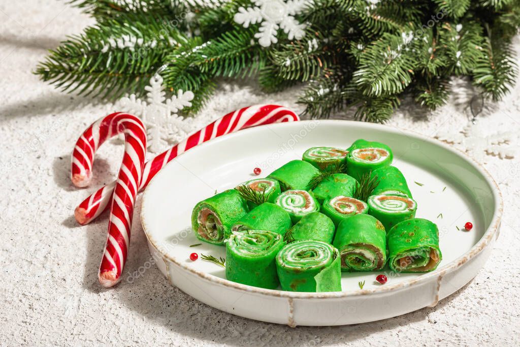 Cold appetizer, decorated in the form of a Christmas tree. Thin crepes, cream cheese, lightly salted salmon, greens, trendy hard light, dark shadow. Festive New Year decor, putty background, close up