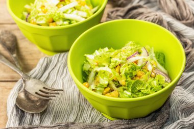 Çin lahanasından lezzetli vejetaryen salatası, tatlı mısır, mor soğan ve sos. Ahşap arka plan, çatal bıçak takımı, eski peçete, kırsal stil, kapat.