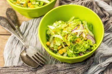 Çin lahanasından lezzetli vejetaryen salatası, tatlı mısır, mor soğan ve sos. Ahşap arka plan, çatal bıçak takımı, eski peçete, kırsal stil, kapat.