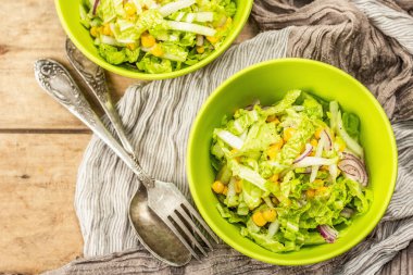 Çin lahanasından lezzetli vejetaryen salatası, tatlı mısır, mor soğan ve sos. Ahşap zemin, çatal bıçak takımı, eski peçete, kırsal stil, üst manzara.