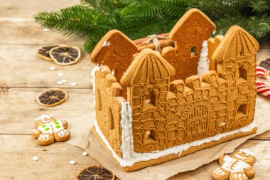 Tatlı kremayla dekore edilmiş zencefilli kek evi. El yapımı, şenlikli yeni yıl dekorasyonu. Geleneksel baharatlar, ahşap arka plan