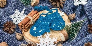 Geleneksel Yeni Yıl dekorasyonuyla örülmüş komik eldivenler. Küçük köknar, örülmüş kar taneleri, fındık, tarçın ve koni. Ahşap tezgah, rahat örgü süveter aranjmanı, afiş