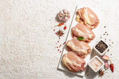 Kemiksiz ve derisiz çiğ tavuk budu. Sağlıklı yemek, baharat ve sarımsak hazırlamak için kullanışlı bir malzeme. Modaya uygun sert ışık, karanlık gölge, aydınlık macun arkaplan, üst görünüm