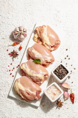 Kemiksiz ve derisiz çiğ tavuk budu. Sağlıklı yemek, baharat ve sarımsak hazırlamak için kullanışlı bir malzeme. Modaya uygun sert ışık, karanlık gölge, aydınlık macun arkaplan, üst görünüm