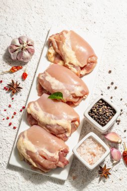 Kemiksiz ve derisiz çiğ tavuk budu. Sağlıklı yemek, baharat ve sarımsak hazırlamak için kullanışlı bir malzeme. Modaya uygun sert ışık, karanlık gölge, aydınlık macun arkaplan, üst görünüm