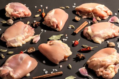 Kemiksiz ve derisiz çiğ tavuk butları. Sağlıklı yemek, baharat ve sarımsak hazırlamak için kullanışlı bir malzeme. Siyah taş arka plan, modaya uygun sert ışık, karanlık gölge, kapat