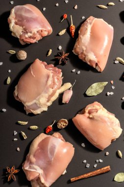 Kemiksiz ve derisiz çiğ tavuk butları. Sağlıklı yemek, baharat ve sarımsak hazırlamak için kullanışlı bir malzeme. Siyah taş arka plan, modaya uygun sert ışık, karanlık gölge, üst görüş