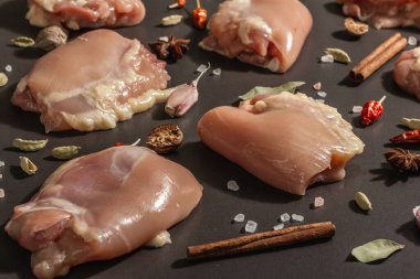 Kemiksiz ve derisiz çiğ tavuk butları. Sağlıklı yemek, baharat ve sarımsak hazırlamak için kullanışlı bir malzeme. Siyah taş arka plan, modaya uygun sert ışık, karanlık gölge, kapat