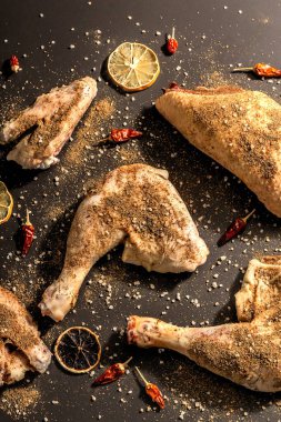 Çiğ tavuk budu ve baharat. Sağlıklı yemek hazırlamak için kullanışlı bir malzeme. Siyah taş arka plan, modaya uygun sert ışık, karanlık gölge, üst görüş