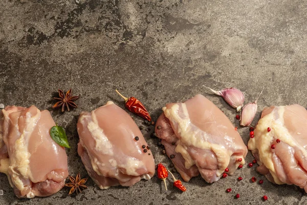 Kemiksiz ve derisiz çiğ tavuk budu. Sağlıklı yemek, baharat ve sarımsak hazırlamak için kullanışlı bir malzeme. Koyu taş arkaplan, üst görünüm