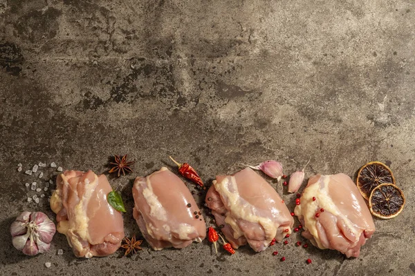 Kemiksiz ve derisiz çiğ tavuk budu. Sağlıklı yemek, baharat ve sarımsak hazırlamak için kullanışlı bir malzeme. Koyu taş arkaplan, üst görünüm