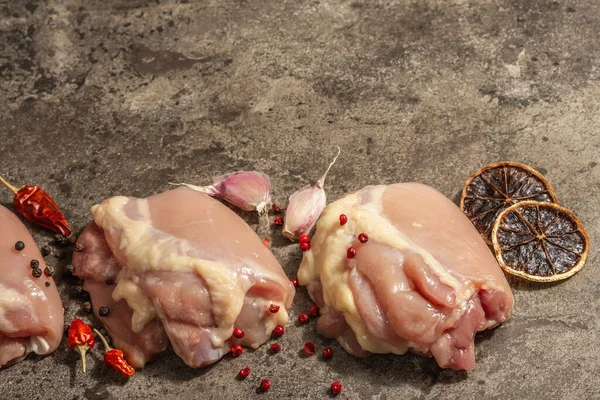 Kemiksiz ve derisiz çiğ tavuk budu. Sağlıklı yemek, baharat ve sarımsak hazırlamak için kullanışlı bir malzeme. Koyu taş arkaplan, üst görünüm