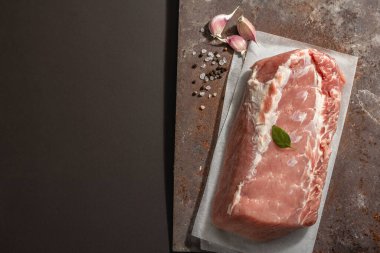 Baharatlı çiğ domuz filetosu. Paslı metal standında büyük bir parça et, siyah taş beton arka plan. Modaya uygun sert ışık, koyu gölge, üst manzara