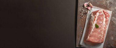 Baharatlı çiğ domuz filetosu. Paslı metal standında büyük bir parça et, siyah taş beton arka plan. Modaya uygun sert ışık, koyu gölge, afiş biçimi