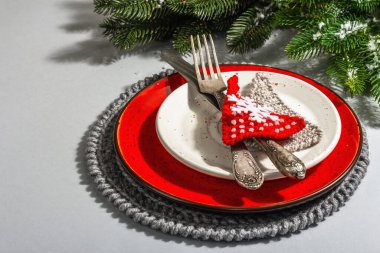 Noel sofrası. Klasik çatal bıçaklı kırmızı seramik tabak, köknar ağacı dalları ve şenlikli aksesuarlar. Modern sert ışık, karanlık gölge. Yaratıcı düz alan, gri arkaplan, kopyalama alanı
