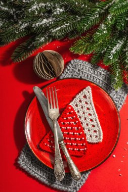 Yılbaşı sofrasını kırmızı tonlarda çatal bıçak setiyle servis etmiş. Evergreen dalları, örülmüş köknar ağaçları, yapay kar. Modern sert ışık, karanlık gölge. Düz konum, kırmızı arkaplan, üst görünüm