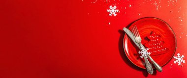 Yılbaşı sofrasını kırmızı tonlarda çatal bıçak setiyle servis etmiş. Tığ işi köknar ağacı, yapay kar. Modern sert ışık, karanlık gölge. Düz konum, kırmızı arkaplan, pankart biçimi