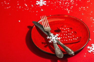Yılbaşı sofrasını kırmızı tonlarda çatal bıçak setiyle servis etmiş. Tığ işi köknar ağacı, yapay kar. Modern sert ışık, karanlık gölge. Düz konum, kırmızı arkaplan, kapat