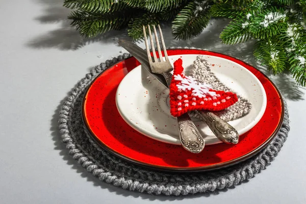 Noel sofrası. Klasik çatal bıçaklı kırmızı seramik tabak, köknar ağacı dalları ve şenlikli aksesuarlar. Modern sert ışık, karanlık gölge. Yaratıcı düz döşeme, gri arkaplan, kapat