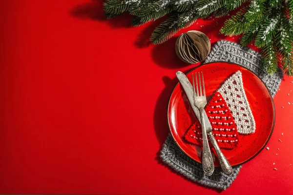 Yılbaşı sofrasını kırmızı tonlarda çatal bıçak setiyle servis etmiş. Evergreen dalları, örülmüş köknar ağaçları, yapay kar. Modern sert ışık, karanlık gölge. Düz konum, kırmızı arkaplan, üst görünüm