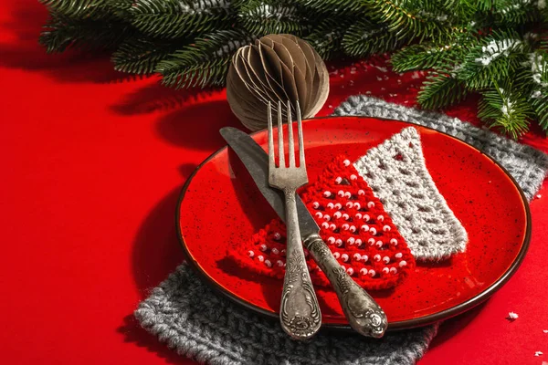 ヴィンテージの刃物で赤いトーンでクリスマステーブルの設定を提供しています 常緑の枝 松葉杖モミの木 人工雪 現代のハードライト 暗い影 フラットレイアウト 赤の背景 コピースペース — ストック写真