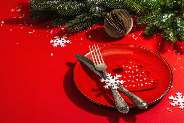 Yılbaşı sofrasını kırmızı tonlarda çatal bıçak setiyle servis etmiş. Evergreen dalları, örülmüş köknar ağaçları, yapay kar. Modern sert ışık, karanlık gölge. Düz konum, kırmızı arkaplan, kopyalama alanı