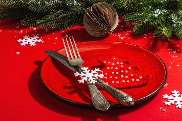Yılbaşı sofrasını kırmızı tonlarda çatal bıçak setiyle servis etmiş. Evergreen dalları, örülmüş köknar ağaçları, yapay kar. Modern sert ışık, karanlık gölge. Düz konum, kırmızı arkaplan, kapat