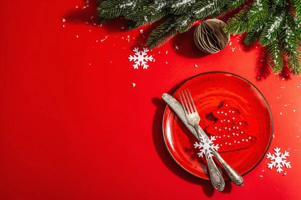 ヴィンテージの刃物で赤いトーンでクリスマステーブルの設定を提供しています 常緑の枝 松葉杖モミの木 人工雪 現代のハードライト 暗い影 フラットレイアウト 赤の背景 トップビュー — ストック写真