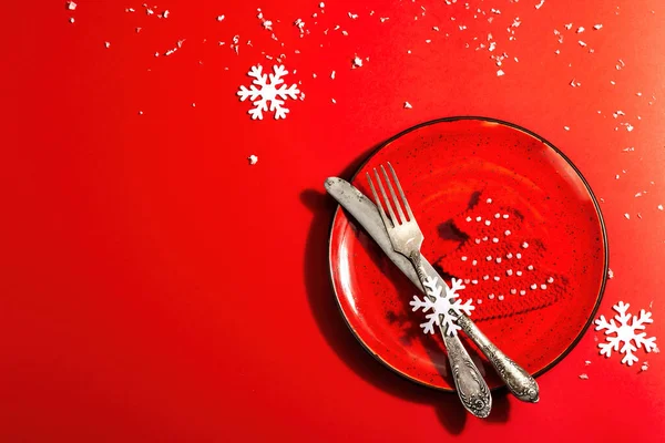 Yılbaşı sofrasını kırmızı tonlarda çatal bıçak setiyle servis etmiş. Tığ işi köknar ağacı, yapay kar. Modern sert ışık, karanlık gölge. Düz konum, kırmızı arkaplan, üst görünüm