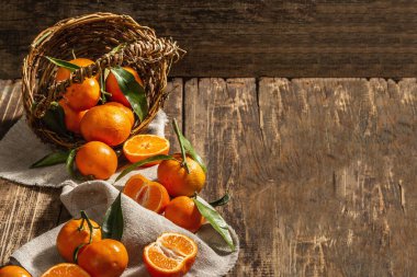Mandalinalar sepetten düşüyor. Yeşil yapraklı portakallar, mandalinalar, turunçgiller. Ahşap arkaplan, rustik biçim, kopyalama alanı