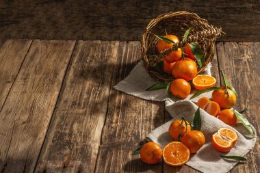 Mandalinalar sepetten düşüyor. Yeşil yapraklı portakallar, mandalinalar, turunçgiller. Ahşap arkaplan, rustik biçim, kopyalama alanı