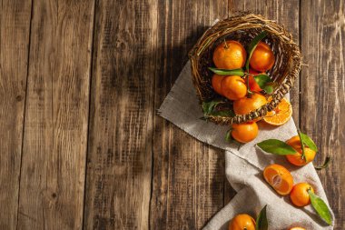 Mandalinalar sepetten düşüyor. Yeşil yapraklı portakallar, mandalinalar, turunçgiller. Ahşap arkaplan, köy tarzı, üst görünüm