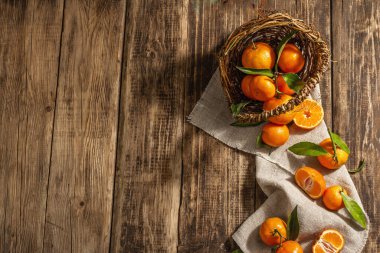 Mandalinalar sepetten düşüyor. Yeşil yapraklı portakallar, mandalinalar, turunçgiller. Ahşap arkaplan, köy tarzı, üst görünüm