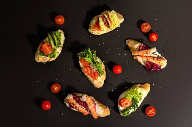 Assorted open sandwiches with salted salmon, shrimps, cream cheese, salad leaves and cucumber. Seafood, healthy food. Black stone concrete background, hard light, dark shadow, top view