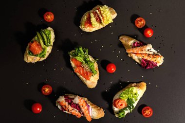 Assorted open sandwiches with salted salmon, shrimps, cream cheese, salad leaves and cucumber. Seafood, healthy food. Black stone concrete background, hard light, dark shadow, top view