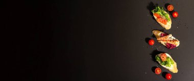 Assorted open sandwiches with salted salmon, shrimps, cream cheese, salad leaves and cucumber. Seafood, healthy food. Black stone concrete background, hard light, dark shadow, banner format