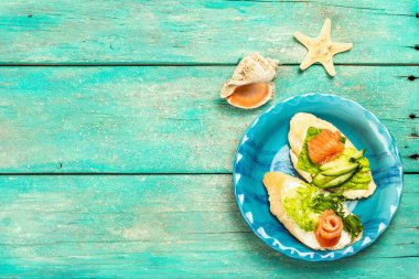 Open sandwiches with salted salmon, cream cheese, salad leaves and cucumber. Seafood, healthy food. Nautical wooden background, sea decor, top view