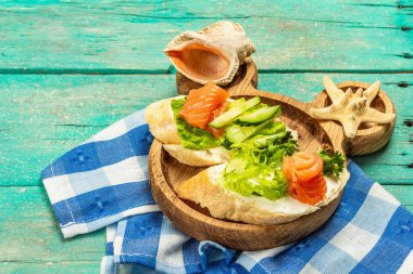 Open sandwiches with salted salmon, cream cheese, salad leaves and cucumber. Seafood, healthy food for children. Nautical wooden background, sea decor, copy space