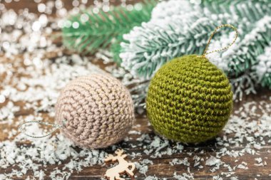 Crocheted Christmas balls and holiday decor. Snow-covered fir tree branches, wooden background. Festive greeting card concept, wallpaper, close up