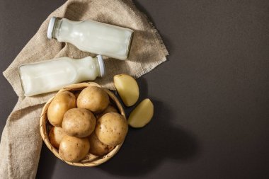 Alternatif patates sütü, güncel sütsüz içecek. Laktozsuz vejetaryen bitki içeceği, sebze ve kuru toz. Modern sert ışık, karanlık gölge, siyah taş zemin, üst görünüm