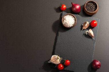 Yemek pişirme konsepti. Seramik standı, domates kirazı, sarımsak, deniz tuzu, biber ve mor soğan. Modaya uygun sert ışık, karanlık gölge, siyah taş beton arka plan, üst manzara.