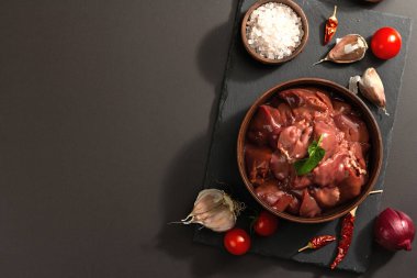 Seramik kasede çiğ tavuk ciğeri. Baharatlı taze yiyecek. Modaya uygun sert ışık, karanlık gölge. Siyah taş arkaplan, üst görünüm