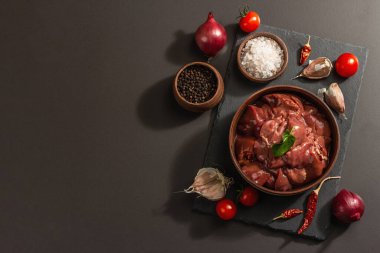 Seramik kasede çiğ tavuk ciğeri. Baharatlı taze yiyecek. Modaya uygun sert ışık, karanlık gölge. Siyah taş arkaplan, üst görünüm