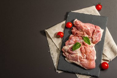 Çiğ hindi budu ve baharat. Seramik tezgahta taze kemiksiz et. Modern sert ışık, karanlık gölge. Siyah taş arkaplan, üst görünüm
